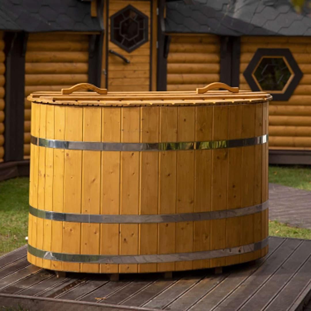 Ovale Holzbadewanne mit Holzdeckel auf einem Holzdeck vor einem Blockhaus